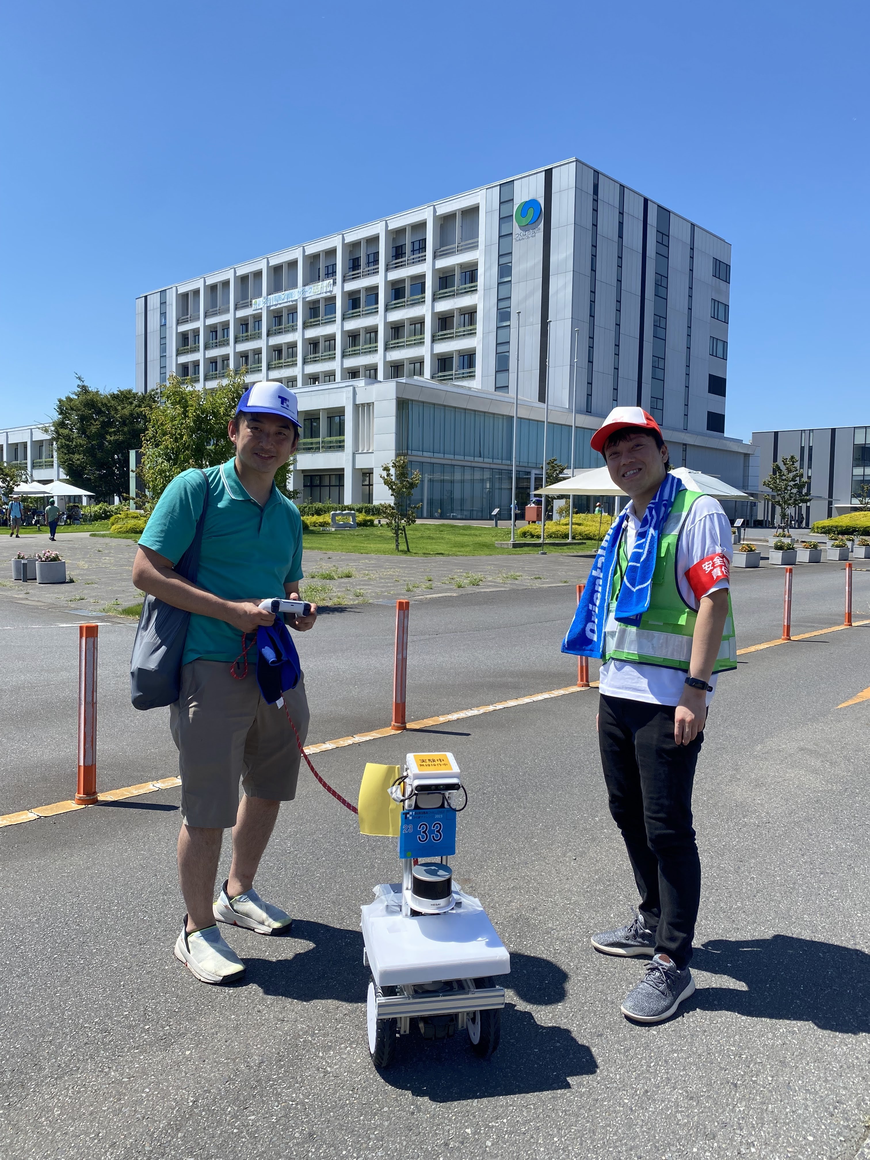 田中さんと男性が自律ロボットを挟んで立つ屋外の写真