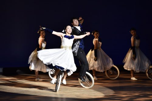 華やかな衣装で一輪車に乗り演技をしている5人の男女の写真